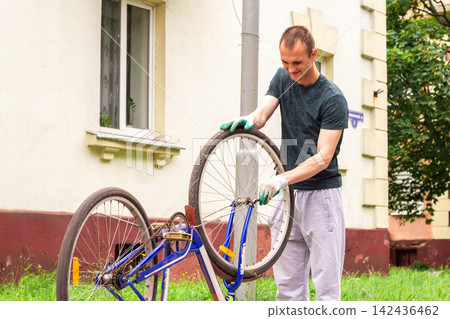 Man flipping bike upside down before house. Checking wheels and chain for damage. Bike repair shows self reliance. Seasonal preparation for summer rides Man flipping bike upside down before house. Checking wheels and chain for damage. Bike repair shows self reliance. Seasonal preparation for summer rides 142436462