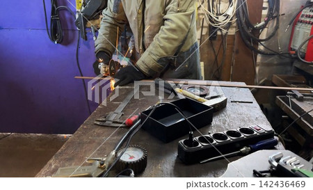 Professional repairman sawing metal construction with a circular saw at garage. Adult craftsman cuts iron using electric grind wheel and sparks flying around at workshop. Slow motion Professional repairman sawing metal construction with a circular saw at garage. Adult craftsman cuts iron using electric grind wheel and sparks flying around at workshop. Slow motion 142436469