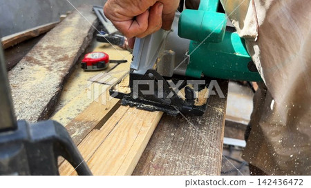 Arms of professional repairman sawing wooden construction with a circular saw at construction. Male hands of adult craftsman cuts wood using electric grind wheel at the site. Slow motion Arms of professional repairman sawing wooden construction with a circular saw at construction. Male hands of adult craftsman cuts wood using electric grind wheel at the site. Slow motion 142436472
