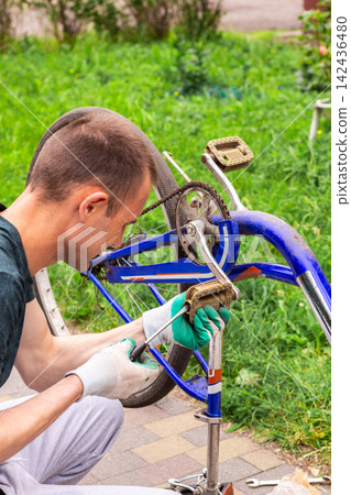 Man examining bicycle wheel near house. Personal vehicle maintenance without service center. Wheel alignment and preparing for upcoming rides Man examining bicycle wheel near house. Personal vehicle maintenance without service center. Wheel alignment and preparing for upcoming rides 142436480