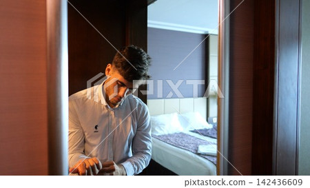 Young businessman adjusting shirt cuffs in front of mirror in modern hotel room or apartment. Handsome entrepreneur preparing for business meeting or formal event showing professional lifestyle Young businessman adjusting shirt cuffs in front of mirror in modern hotel room or apartment. Handsome entrepreneur preparing for business meeting or formal event showing professional lifestyle 142436609