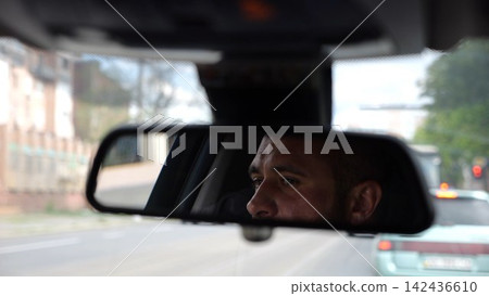 Eyes of male driver reflecting in rearview mirror while riding motor auto. Young man looking concentrated to urban road during operating electric vehicle. Confident guy driving modern car at city 142436610