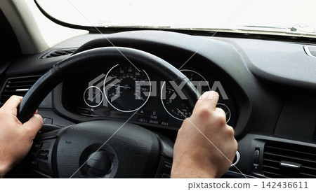 Male arms holds steering wheel while driving a motor car at city. Young man riding on electric automobile at urban road. Driver moving on his electrical auto on route. Slow motion Male arms holds steering wheel while driving a motor car at city. Young man riding on electric automobile at urban road. Driver moving on his electrical auto on route. Slow motion 142436611