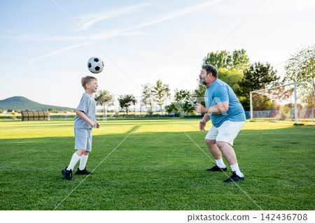 Dad helping young boy improve football technique during training. 142436708