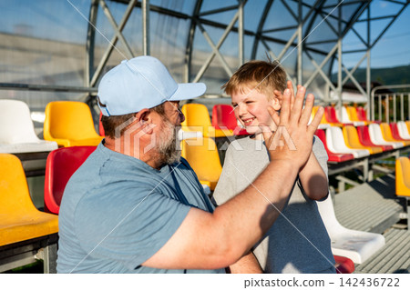 Father and son cheering for football team during match at stadium. Father and son cheering for football team during match at stadium. 142436722
