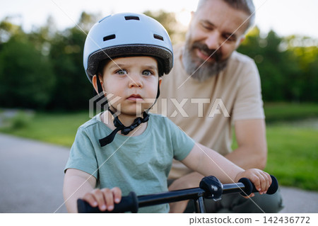 Father teaching toddler son to ride balance bike while wearing safety helmet. Father teaching toddler son to ride balance bike while wearing safety helmet. 142436772