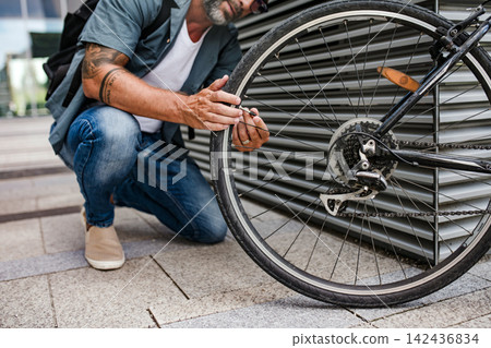 Man fixing bicycle wheel outdoors. 142436834