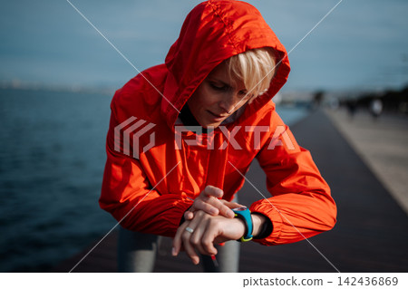 Fit woman setting smartwatch before running on seaside promenade. Fit woman setting smartwatch before running on seaside promenade. 142436869