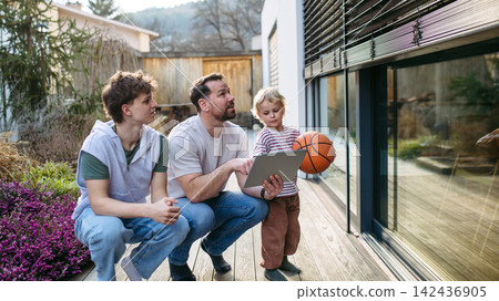 Father controlling smart home exterior blinds using tablet while standing with older and young son. Father controlling smart home exterior blinds using tablet while standing with older and young son. 142436905