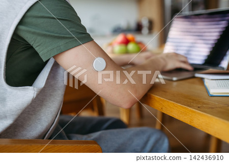 Teen boy with diabetes working on school project on laptop at kitchen table. Teen boy with diabetes working on school project on laptop at kitchen table. 142436910