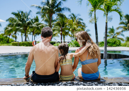 Family relaxing by tropical resort pool, child with diabetes wears glucose monitor. Family relaxing by tropical resort pool, child with diabetes wears glucose monitor. 142436936