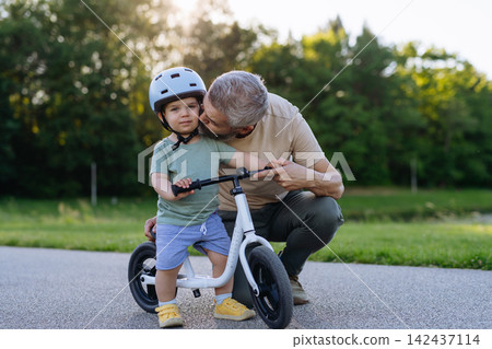 Dad encouraging young child to build confidence on balance bike. Dad encouraging young child to build confidence on balance bike. 142437114