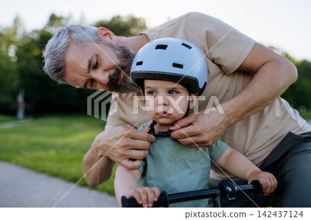Father fastening helmet on toddler son before bike ride. Father fastening helmet on toddler son before bike ride. 142437124
