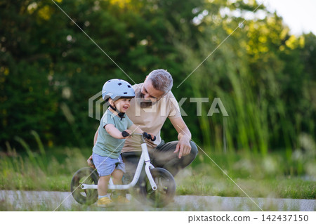 Dad encouraging young child to build confidence on balance bike. Dad encouraging young child to build confidence on balance bike. 142437150