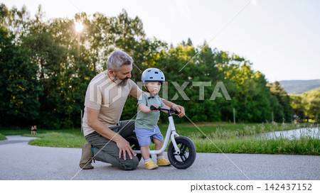 Father teaching toddler son to ride balance bike while wearing safety helmet. Father teaching toddler son to ride balance bike while wearing safety helmet. 142437152
