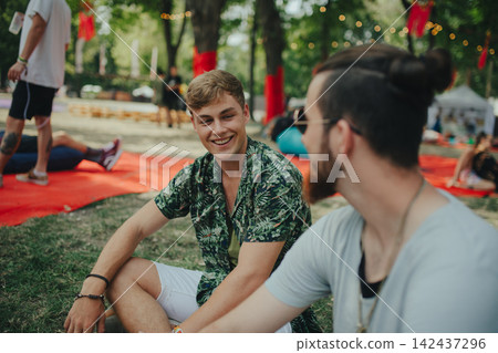 Male friends sitting on ground at summer festival. Male friends sitting on ground at summer festival. 142437296