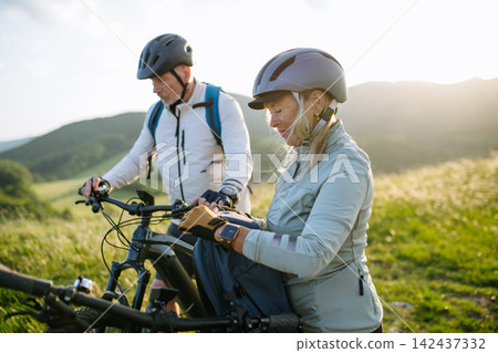 Senior couple taking break during e-bike ride through countryside Senior couple taking break during e-bike ride through countryside 142437332