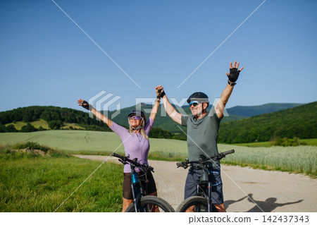 Mature couple celebrating outdoor cycling adventure in nature. Mature couple celebrating outdoor cycling adventure in nature. 142437343