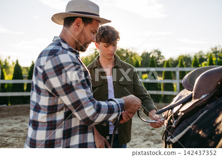 ather and son preparing horse for riding. ather and son preparing horse for riding. 142437352
