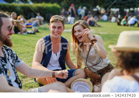 Group of young friends sitting on ground at summer festival. Group of young friends sitting on ground at summer festival. 142437410