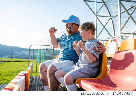 Father and son cheering for football team during match at stadium. Father and son cheering for football team during match at stadium. 142437427