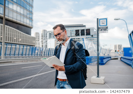 Mature man reading while waiting for bus. Mature man reading while waiting for bus. 142437479
