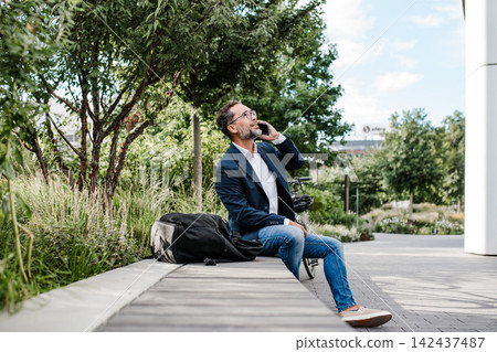 Manager working in urban park, making phone call and sitting on bench. Manager working in urban park, making phone call and sitting on bench. 142437487