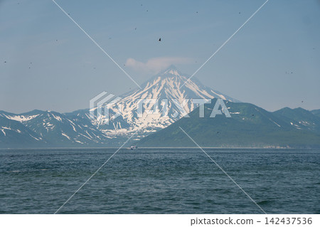 Snow-covered Vilyuchinsky Volcano rises above Pacific Ocean in Avacha Bay, Kamchatka, Russia, under clear blue sky. Volcanic landscape, wilderness, nature travel, adventure Snow-covered Vilyuchinsky Volcano rises above Pacific Ocean in Avacha Bay, Kamchatka, Russia, under clear blue sky. Volcanic landscape, wilderness, nature travel, adventure 142437536