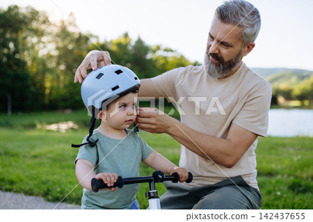 Father fastening helmet on toddler son before bike ride. Father fastening helmet on toddler son before bike ride. 142437655