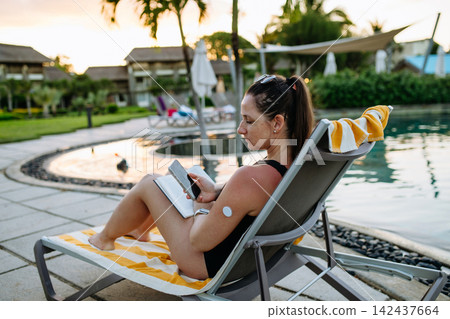 Woman looking at data in diabetes app on smartphone, wearing CGM sensor on arm. Woman looking at data in diabetes app on smartphone, wearing CGM sensor on arm. 142437664