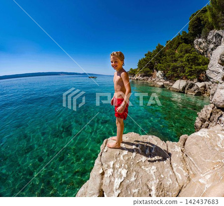 Young boy jumping from coastal rocks into Adriatic Sea on family holiday. Young boy jumping from coastal rocks into Adriatic Sea on family holiday. 142437683