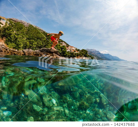 Young boy jumping from coastal rocks into Adriatic Sea on family holiday. Young boy jumping from coastal rocks into Adriatic Sea on family holiday. 142437688
