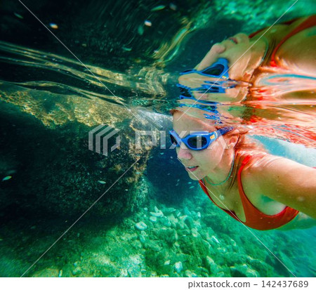 Woman swimming beneath the surface in crystal clear sea water. Woman swimming beneath the surface in crystal clear sea water. 142437689