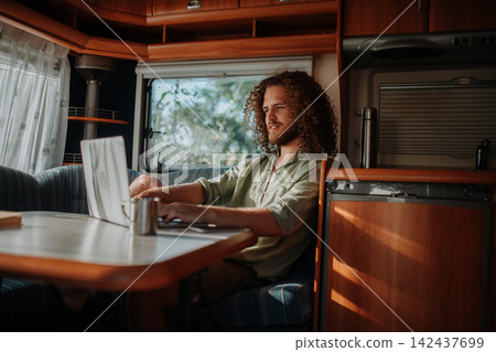 Young man working remotely from caravan. Man using camper as homeoffice, working on notebook. Young man working remotely from caravan. Man using camper as homeoffice, working on notebook. 142437699