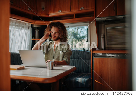 Young man working remotely from caravan. Man using camper as homeoffice, working on notebook. Young man working remotely from caravan. Man using camper as homeoffice, working on notebook. 142437702