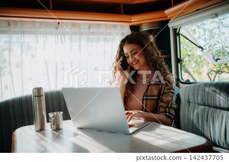 Young beautiful woman is camping in nature, sitting in her caravan and working on a notebook. Caravan as homeoffice, working remotely. Young beautiful woman is camping in nature, sitting in her caravan and working on a notebook. Caravan as homeoffice, working remotely. 142437705