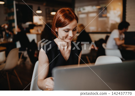 A portrait of woman working remotely from coffee shop, using laptop. A portrait of woman working remotely from coffee shop, using laptop. 142437770