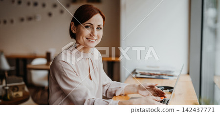 Redhead woman in coffe shop, using laptop and making reservation. Redhead woman in coffe shop, using laptop and making reservation. 142437771