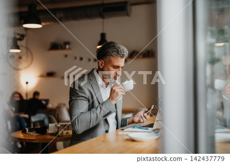 Businessman working remotely from coffee shop, using laptop. Businessman working remotely from coffee shop, using laptop. 142437779