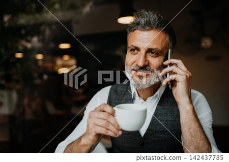 Mature businessman drinking coffee while making phone call with clinet. Mature businessman drinking coffee while making phone call with clinet. 142437785