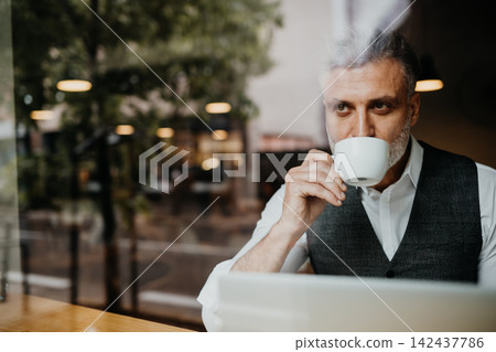 Mature businessman drinking coffee while working on laptop. Mature businessman drinking coffee while working on laptop. 142437786