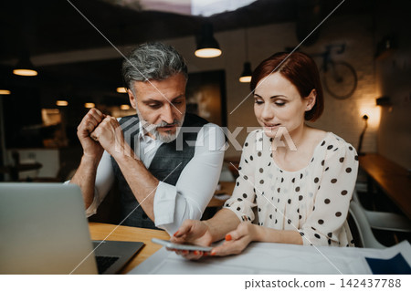 Woman showing project to client during business meeting in a coffee shop. Woman showing project to client during business meeting in a coffee shop. 142437788