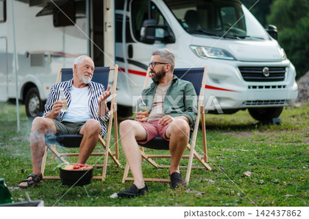 Father and adult son grilling beside camper during family RV vacation. 142437862