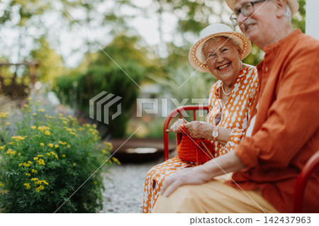 Happy senior couple sitting together in garden bench, smiling and looking at camera. 142437963
