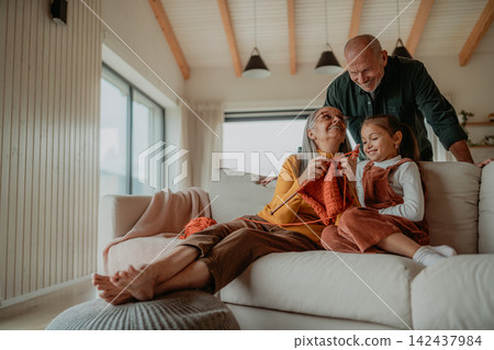 Little girl sitting on sofa with her grandparents and learning to knit indoors at home. Little girl sitting on sofa with her grandparents and learning to knit indoors at home. 142437984