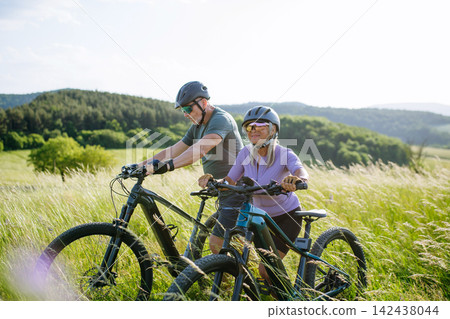 Senior couple taking break during e-bike ride, enjoying nature around them. Senior couple taking break during e-bike ride, enjoying nature around them. 142438044