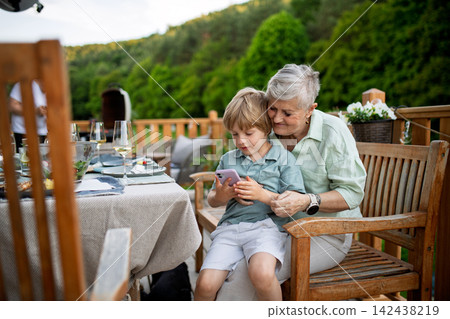 Little boy with his grandmother looking in smartphone during bbq party. Little boy with his grandmother looking in smartphone during bbq party. 142438219