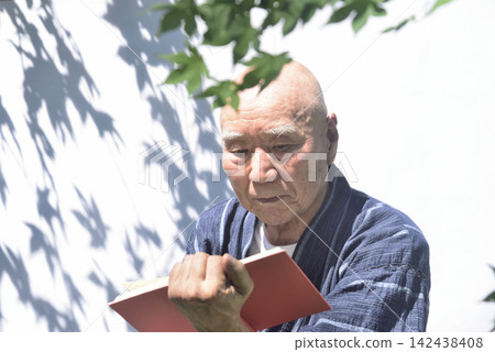 一位住在鄉下的老人在透過樹葉灑下的斑駁陽光下閱讀。 一位住在鄉下的老人在透過樹葉灑下的斑駁陽光下閱讀。 142438408