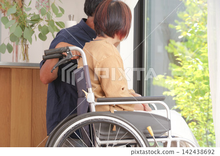 A middle-aged husband comforts his wife in a wheelchair. 142438692