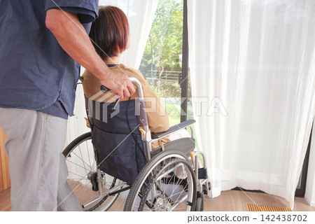 A middle-aged husband comforts his wife in a wheelchair. 142438702